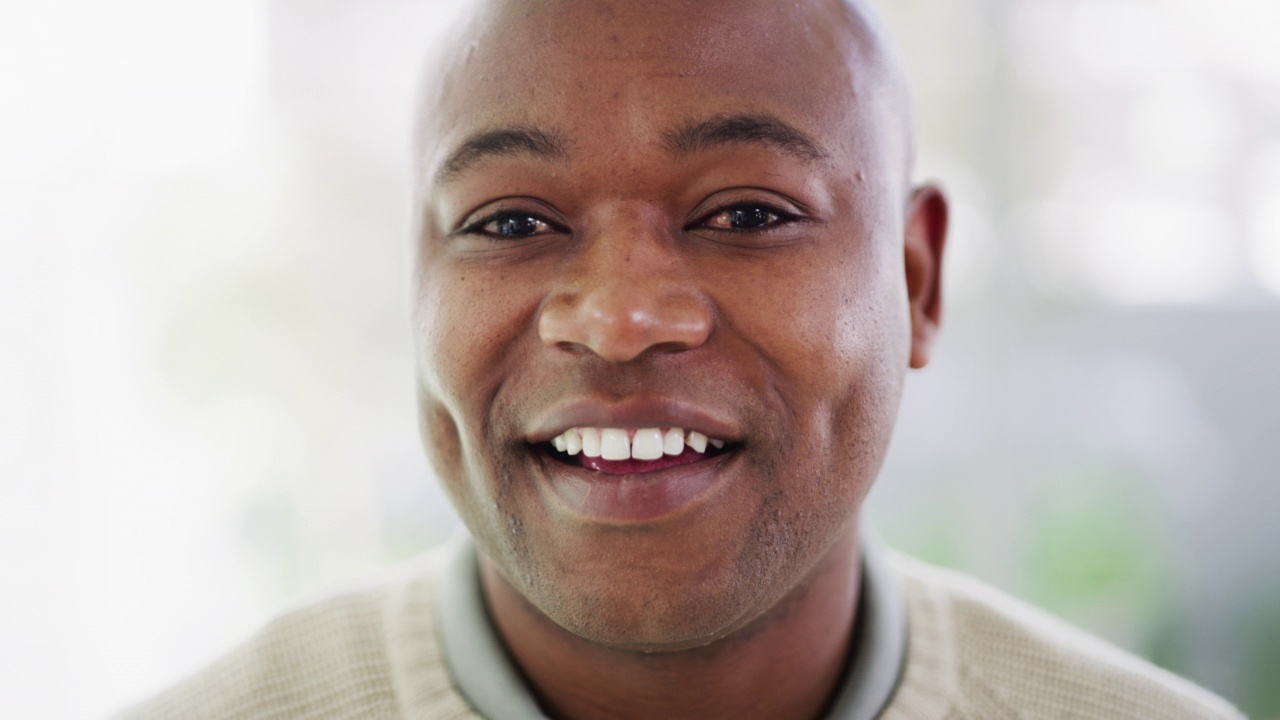 一个微笑的特写，英俊的黑人男子满意他的牙科治疗。一个现代成熟的非洲裔美国人的肖像，灿烂的微笑，在模糊的背景下看起来满足和专注。视频下载