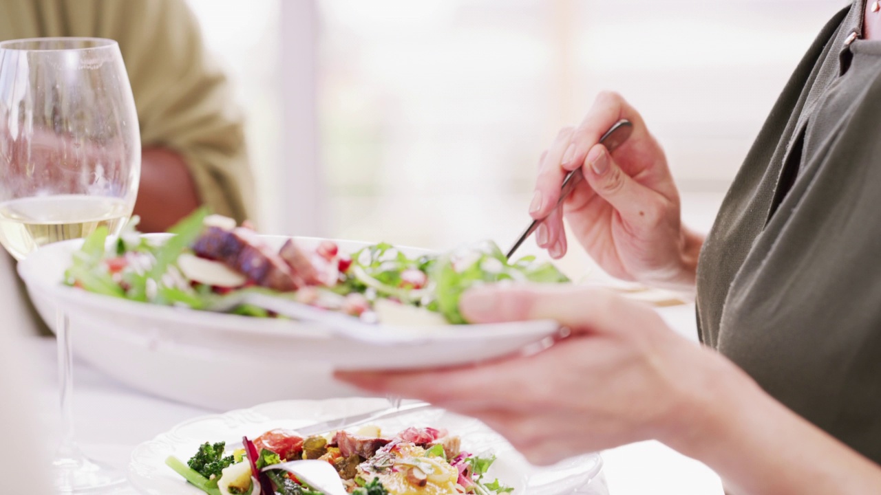 人们在餐桌上吃东西的特写。男男女女在餐厅举行健康晚宴。一群朋友吃着白葡萄酒配蔬菜沙拉。家人和朋友吃饭视频下载