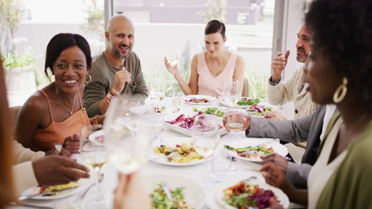 多样化的群体在聚会上享受他们的食物和酒。人们在一张大餐桌上一起吃喝，一起社交。朋友在家里的餐厅吃午饭视频下载