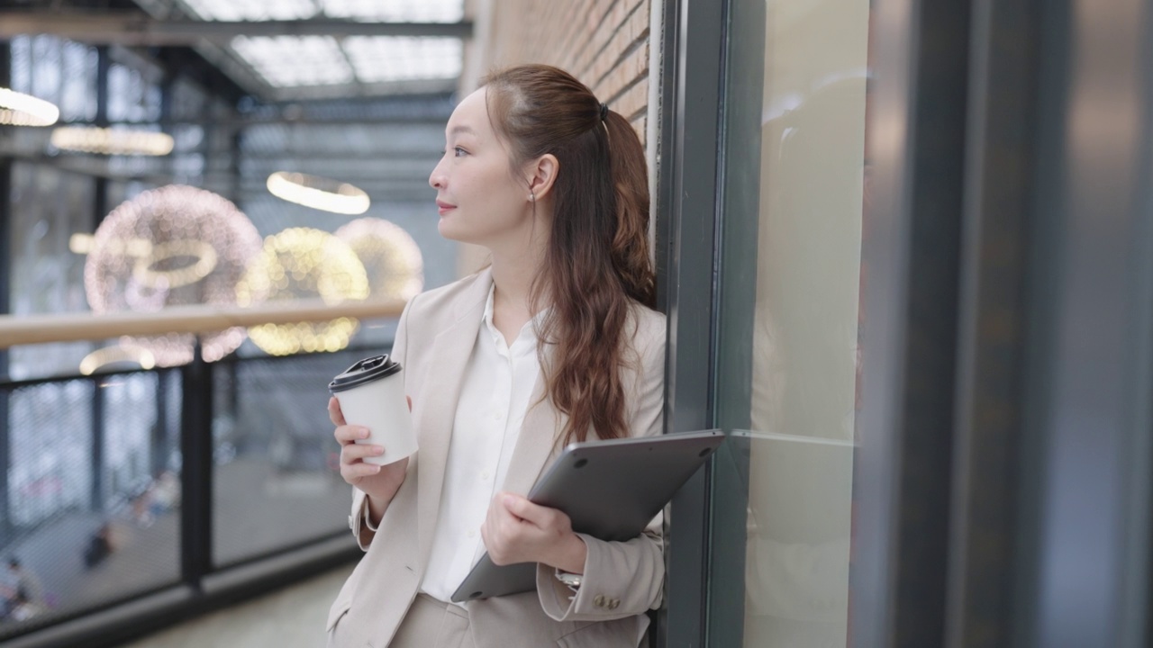 成功的美丽的亚洲商业女性的肖像微笑着看着相机站在办公楼附近，手里拿着一杯热饮和笔记本电脑。商业外场景-东南亚/日本与阿尔法香奈儿。视频素材