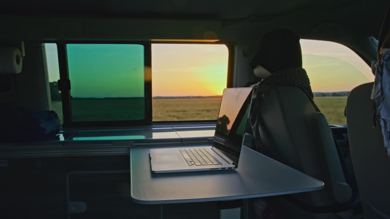 DS笔记本电脑放在一辆露营车里的桌子上，这辆车停在日落时分的乡下视频下载