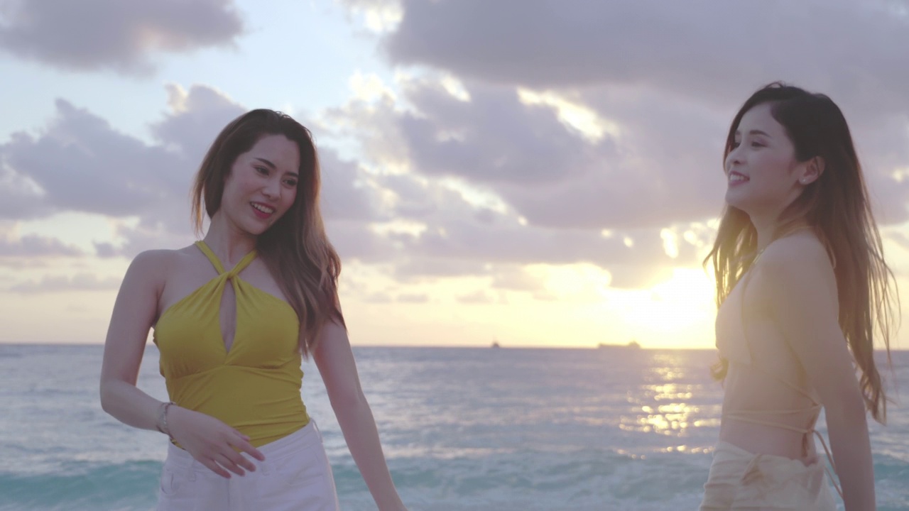 年轻美丽的亚洲女子比基尼裙坐在一起谈论在夏天的热带海滩日落。视频下载