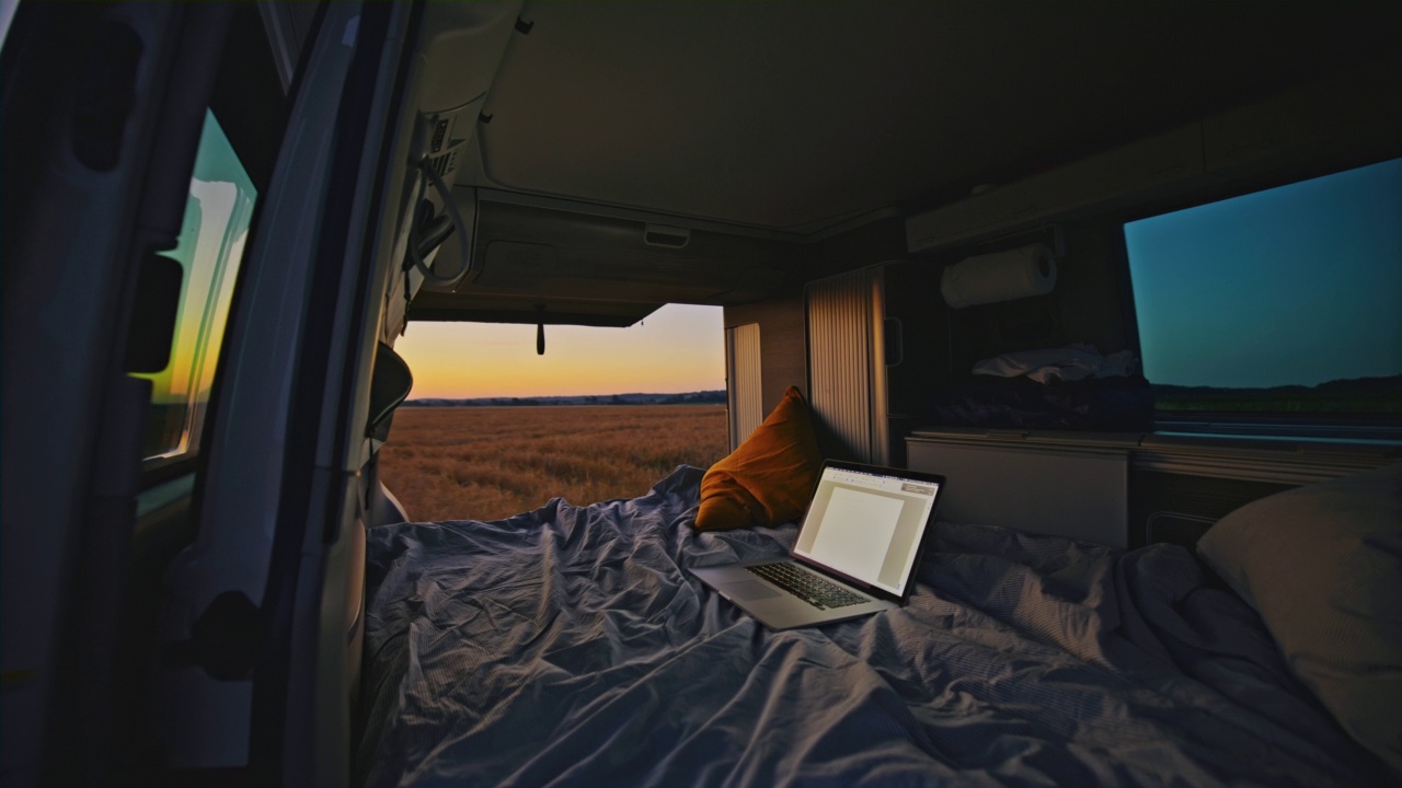DL黄昏时分，露营车停在乡下的某个地方，车上的床上放着笔记本电脑视频下载