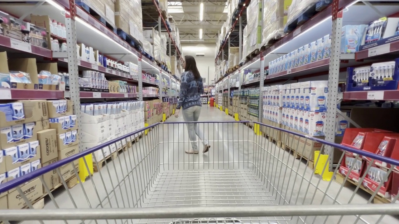 一个男人扛着购物车在大型超市挑选商品，他的妻子在他前面视频下载