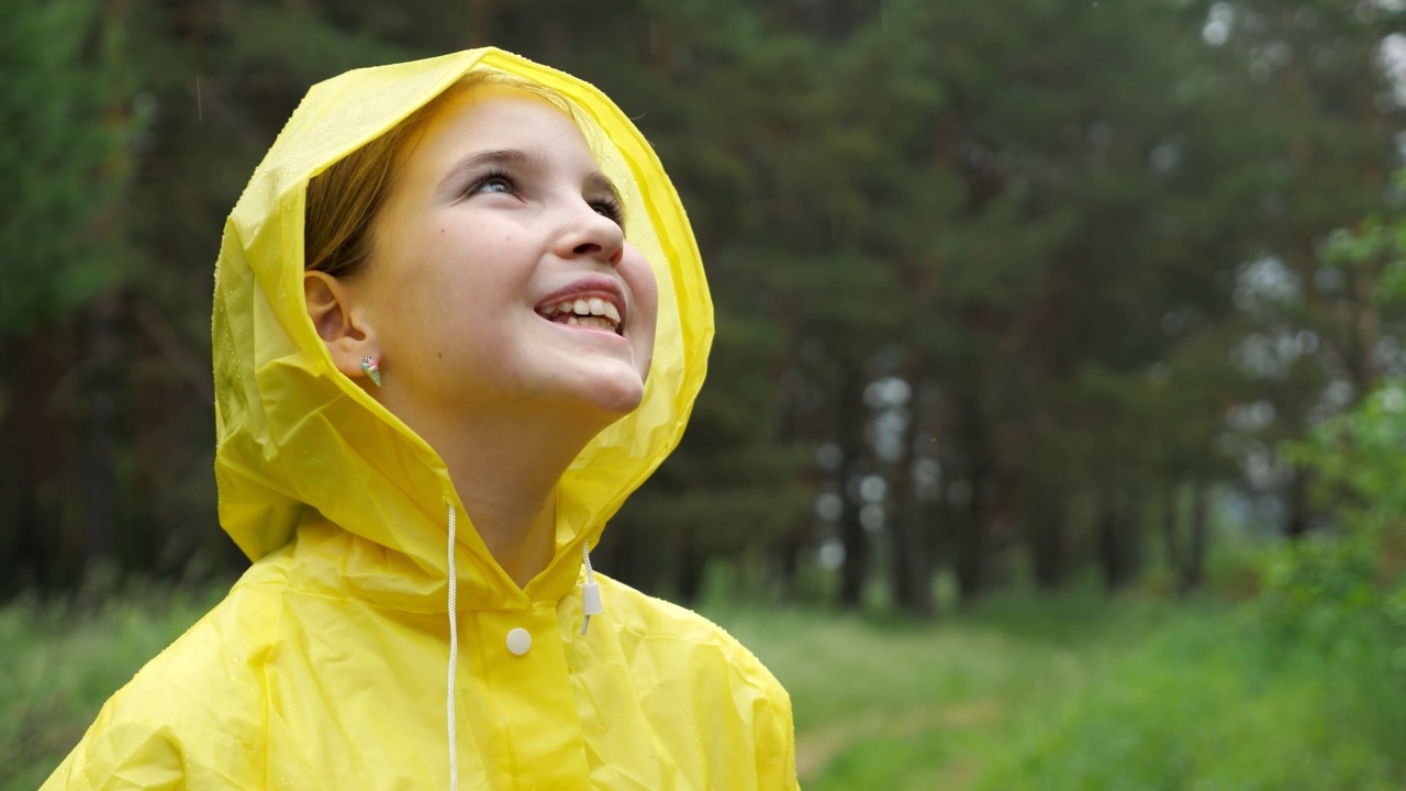 穿着黄色雨衣的快乐女孩在雨天的森林里抬头看。视频素材