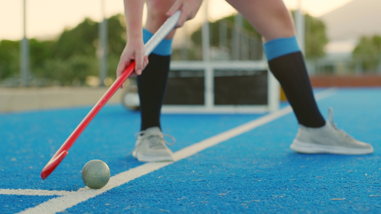 特写运动少年曲棍球运动员站在一个astroturf和推一个球与她的棍子。体育课堂上运动员竞争与得分的低角度视频下载