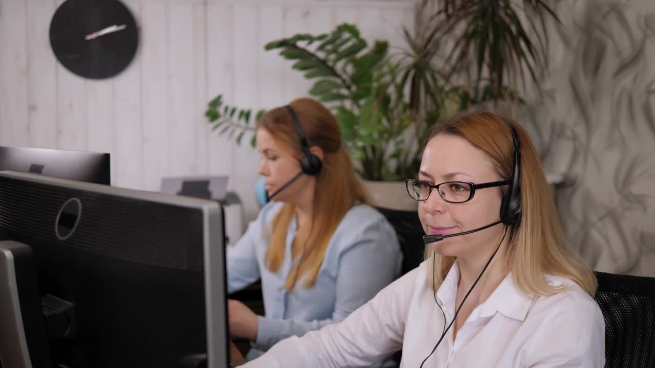 两名戴着耳机的女性呼叫中心接线员在支持服务办公室工作。视频素材