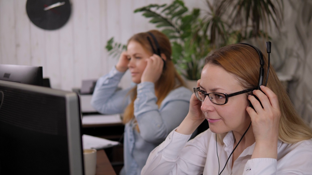 两个女人在开始工作前在办公室戴上耳机的特写。视频素材
