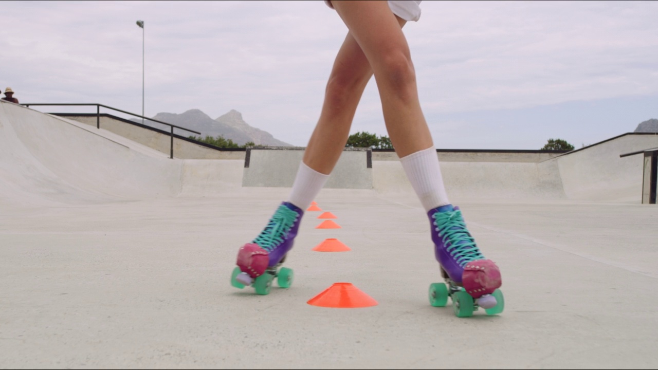 酷的技术滑冰形成模式周围锥在障碍课程，而做之字形的。特写一个滑冰的女人的腿穿着溜冰鞋，有积极的乐趣和显示技巧与copyspace视频素材