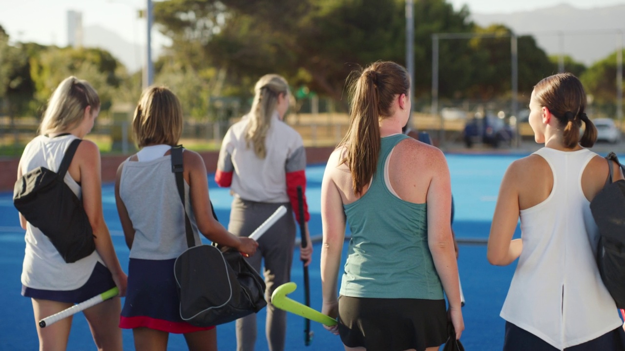 在一个阳光明媚的日子，一群健康活跃的女冰球运动员背着包和曲棍球棒，在球场上进行体育训练后一边说话一边走路。团队对话和建立联系视频下载