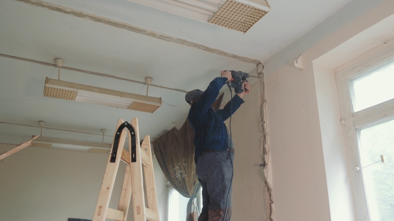 在修理房间时，建筑工人在墙上钻了一个洞。恢复和恢复房间。一名男电工在混凝土墙上钻出一条铺设电缆的轨道。视频素材