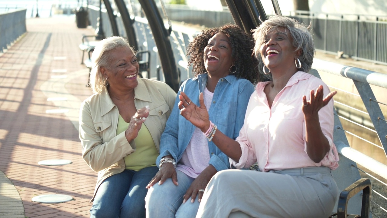 三名非裔美国老年女性在公园长椅上大笑视频素材