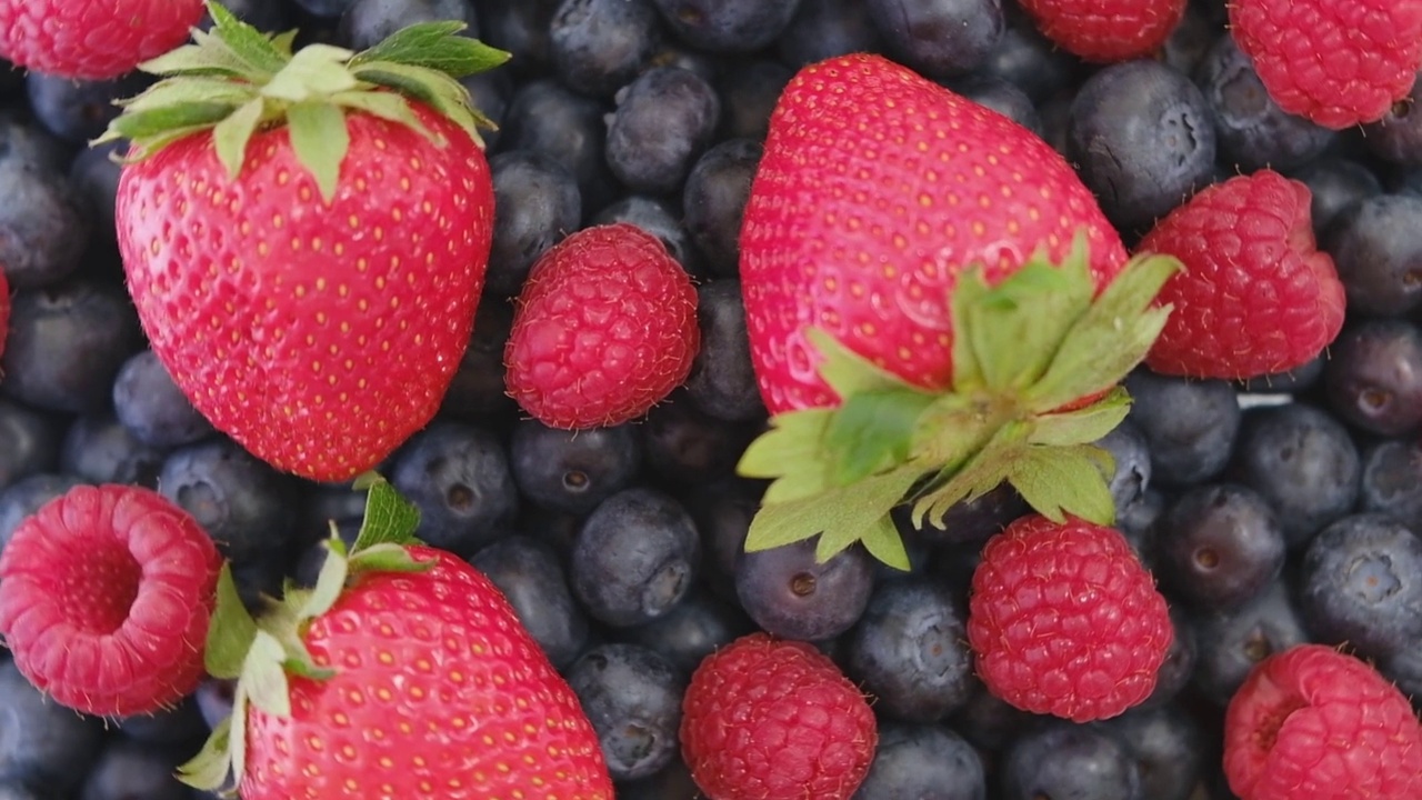 蓝莓，草莓和覆盆子，旋转背景。特写镜头。蓝莓和树莓与绿叶旋转背景。视频下载