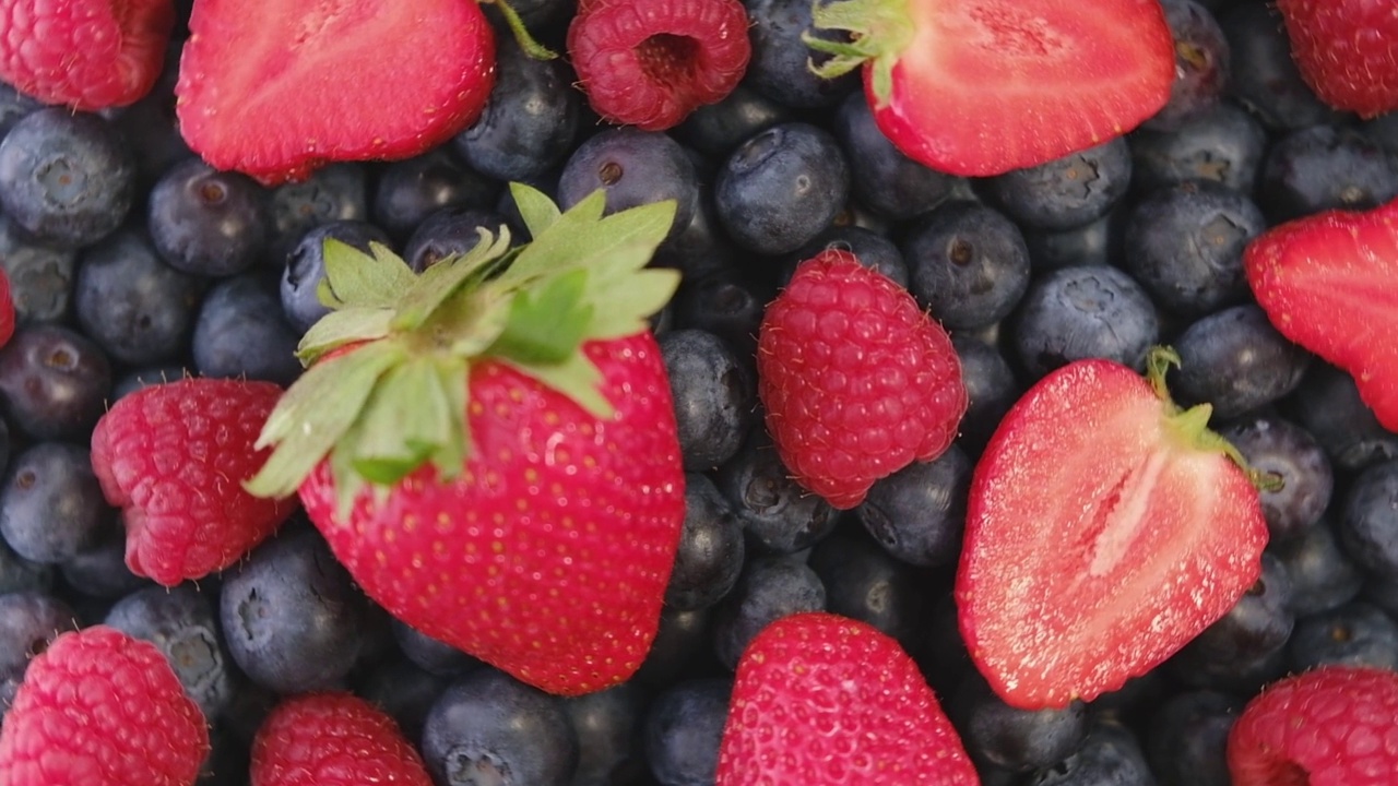 蓝莓，草莓和覆盆子，旋转背景。特写镜头。蓝莓和树莓与绿叶旋转背景。视频下载
