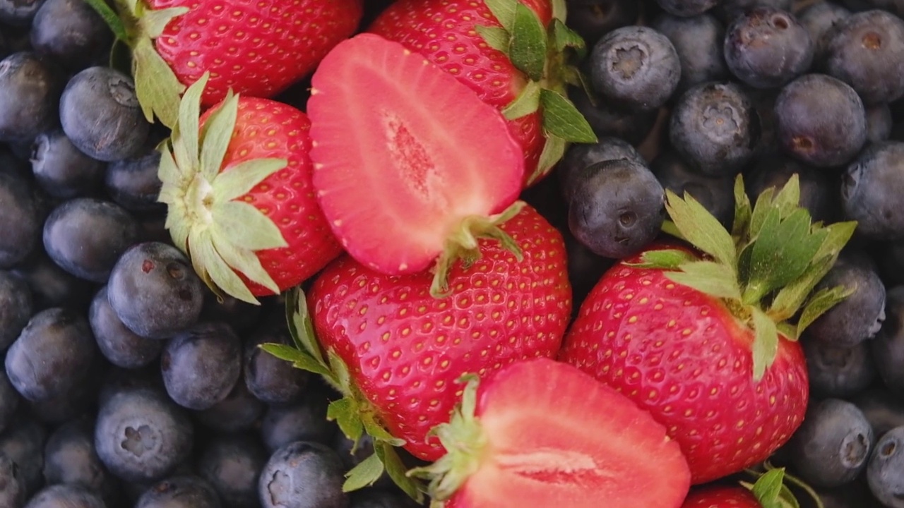 蓝莓和草莓，旋转背景。特写镜头。蓝莓和树莓与绿叶旋转背景。特写镜头。视频下载