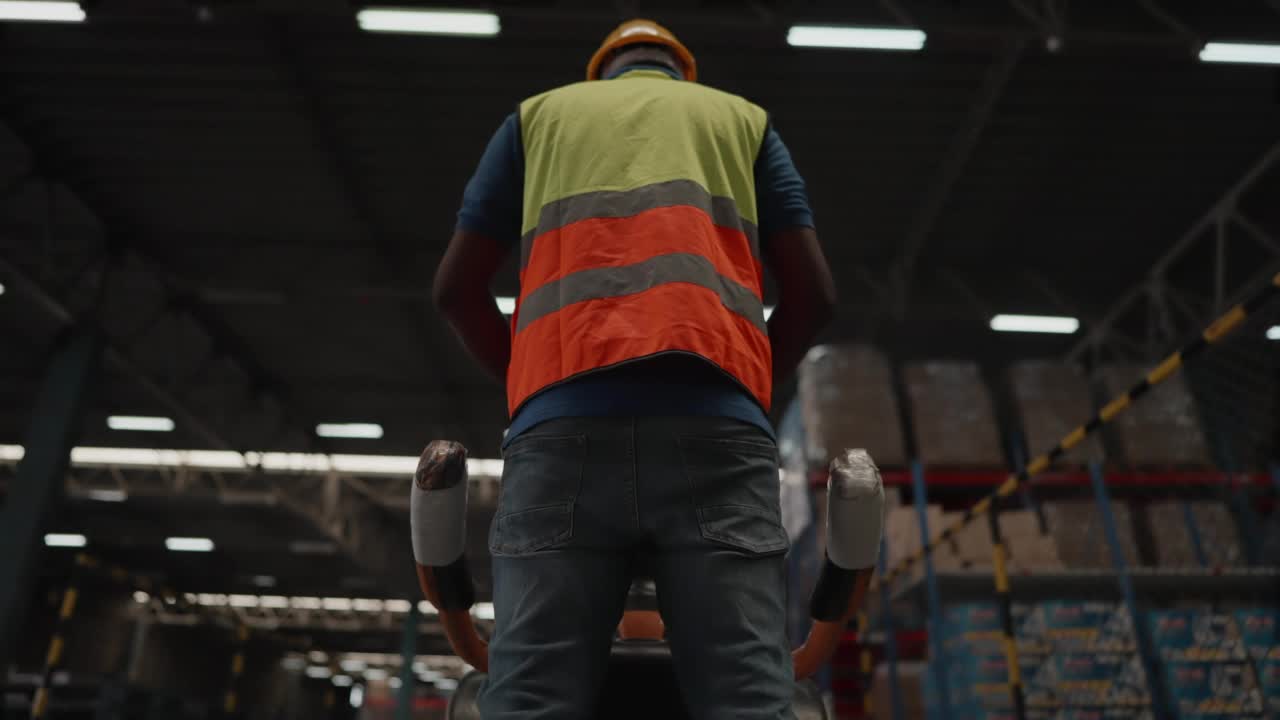 职业男性工人戴着安全帽，在摆满货架的零售仓库用托盘卡车和叉车移动库存，货物装在纸箱里，包装在托盘上。产品配送物流中心工作人员。视频素材