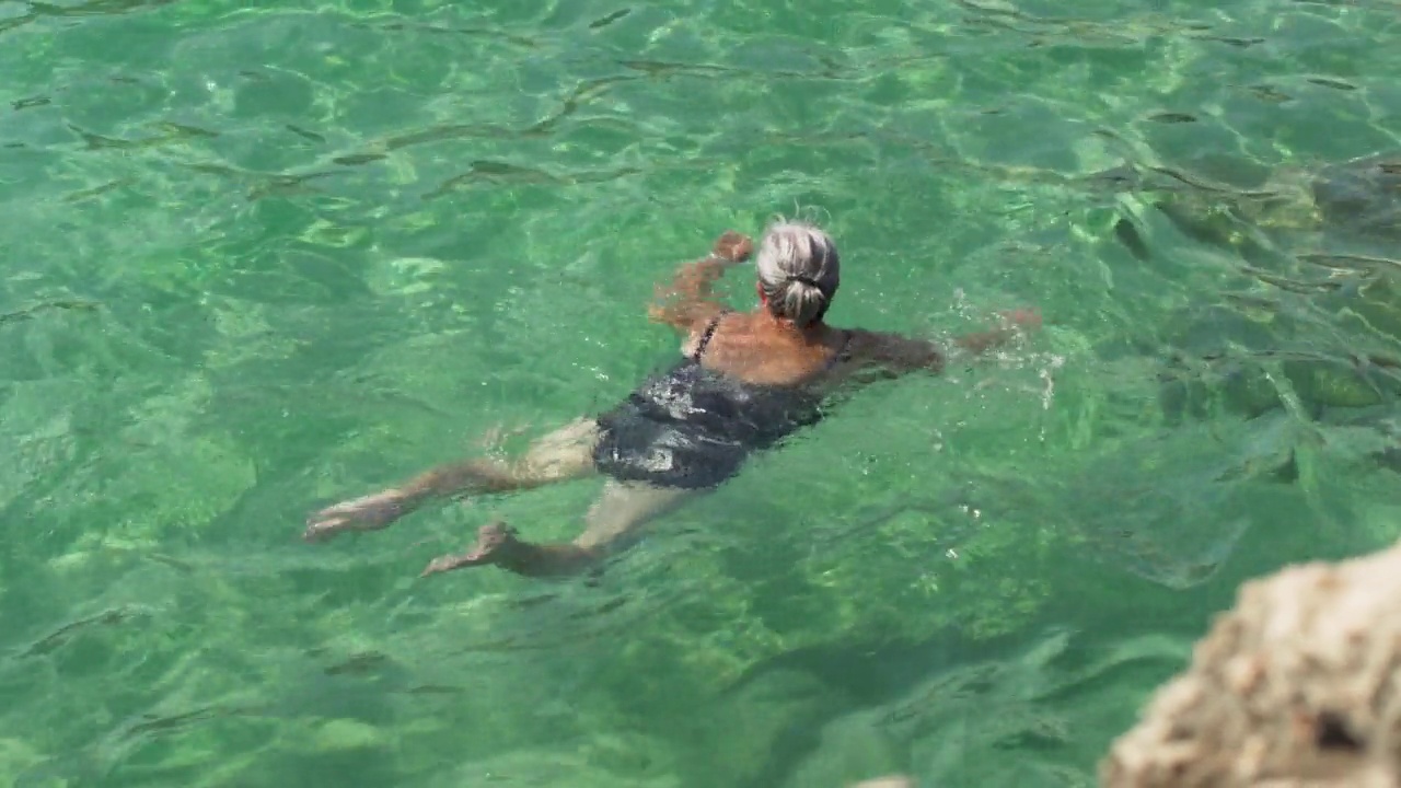 白发苍苍的老年老妇，游在平静清澈的碧绿大海中，俯视视频素材