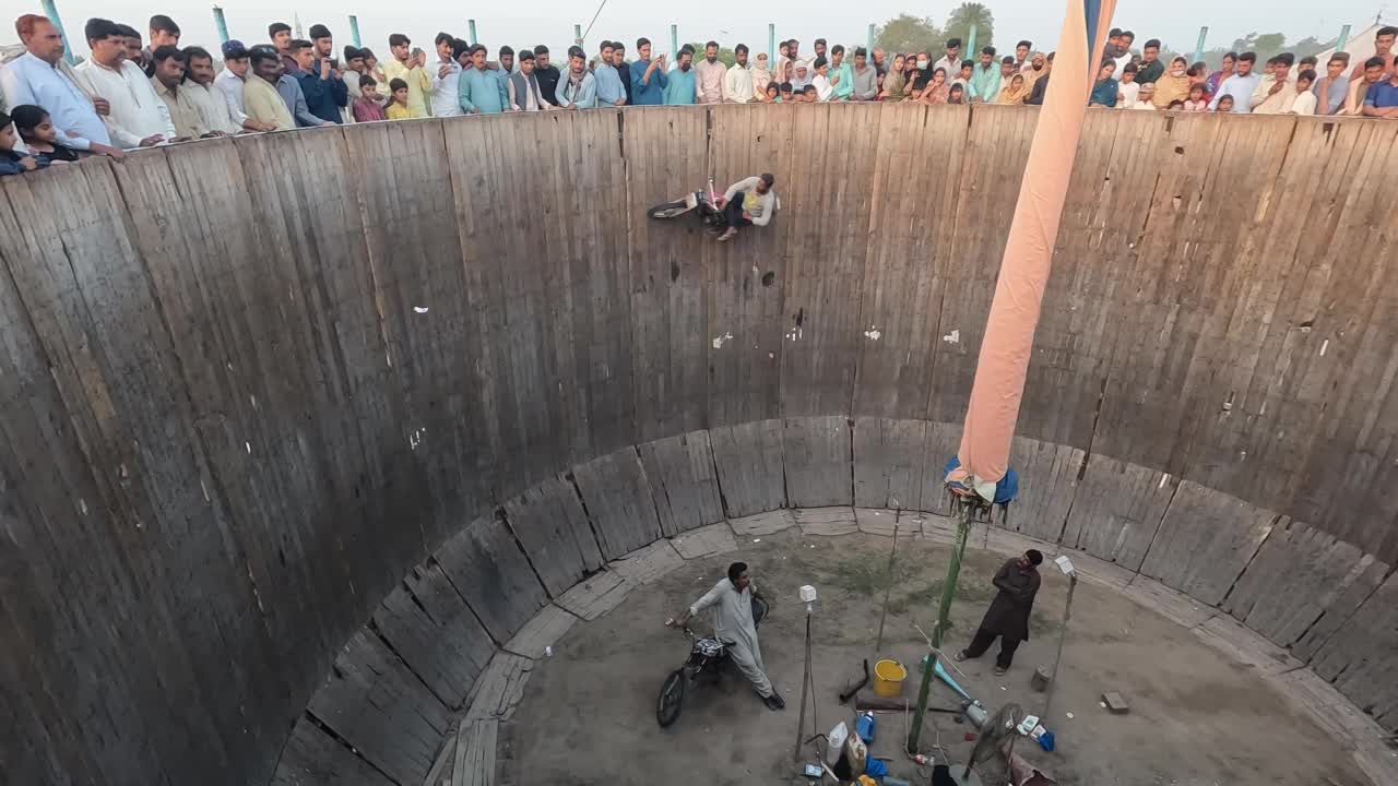 在一个村庄的传统春节期间，特技自行车手们在死亡之井的顶部表演，观众们正在观看他们。视频下载