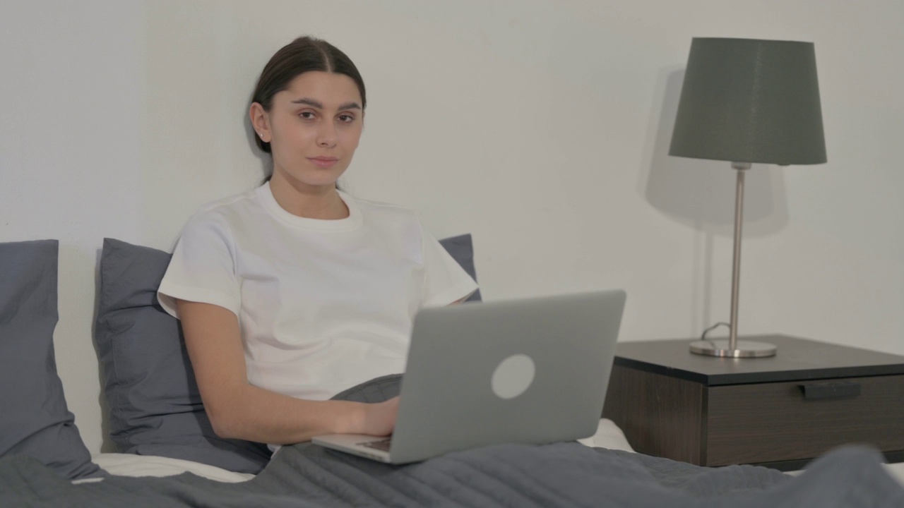 西班牙裔女性在床上使用笔记本电脑时看着相机视频素材