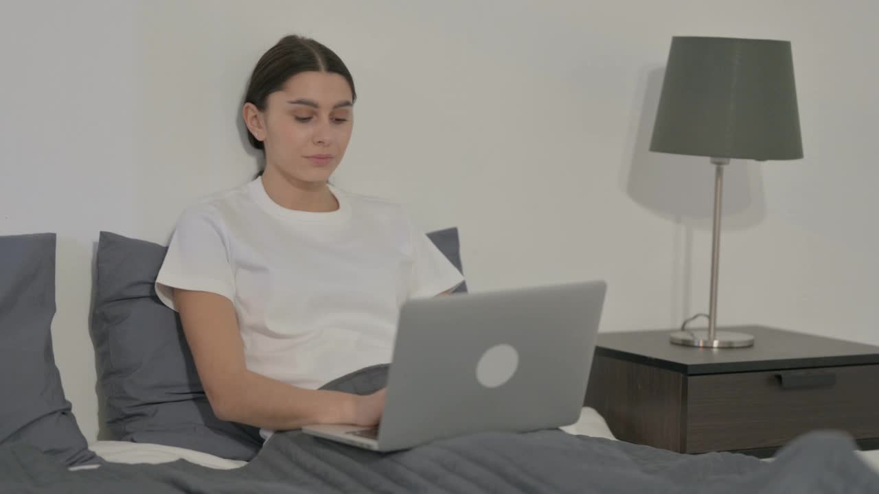 西班牙女性在床上使用笔记本电脑时对着相机微笑视频素材