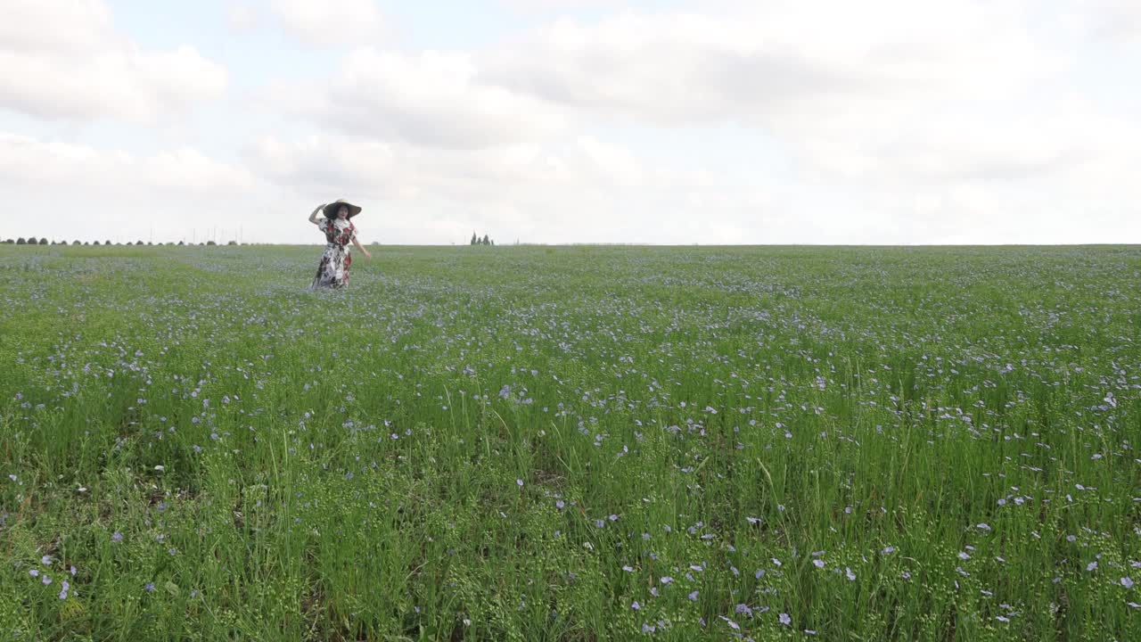夏天，年轻的女孩戴着大帽子在开花的亚麻地里奔跑。4 k的决议视频下载