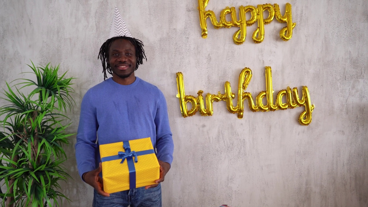 一个年轻黑人男子手持生日礼物的肖像视频素材