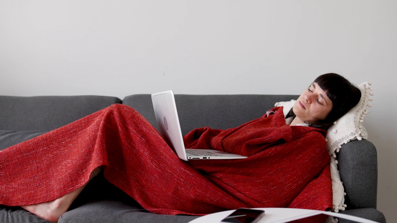 疲惫的女人用笔记本电脑躺在沙发上裹着毯子视频下载