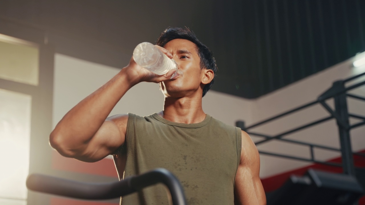 低角度拍摄的亚洲年轻人在健身房训练后喝水，运动后清爽的冷饮。视频素材