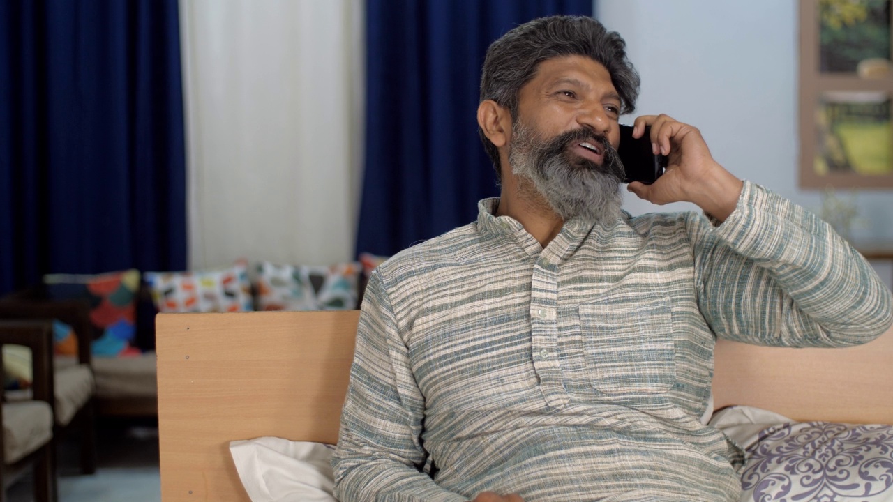 一个兴高采烈的印度中年男子正在用手机聊天——他笑着，神情激动，灰白的头发，灰白的胡须视频素材