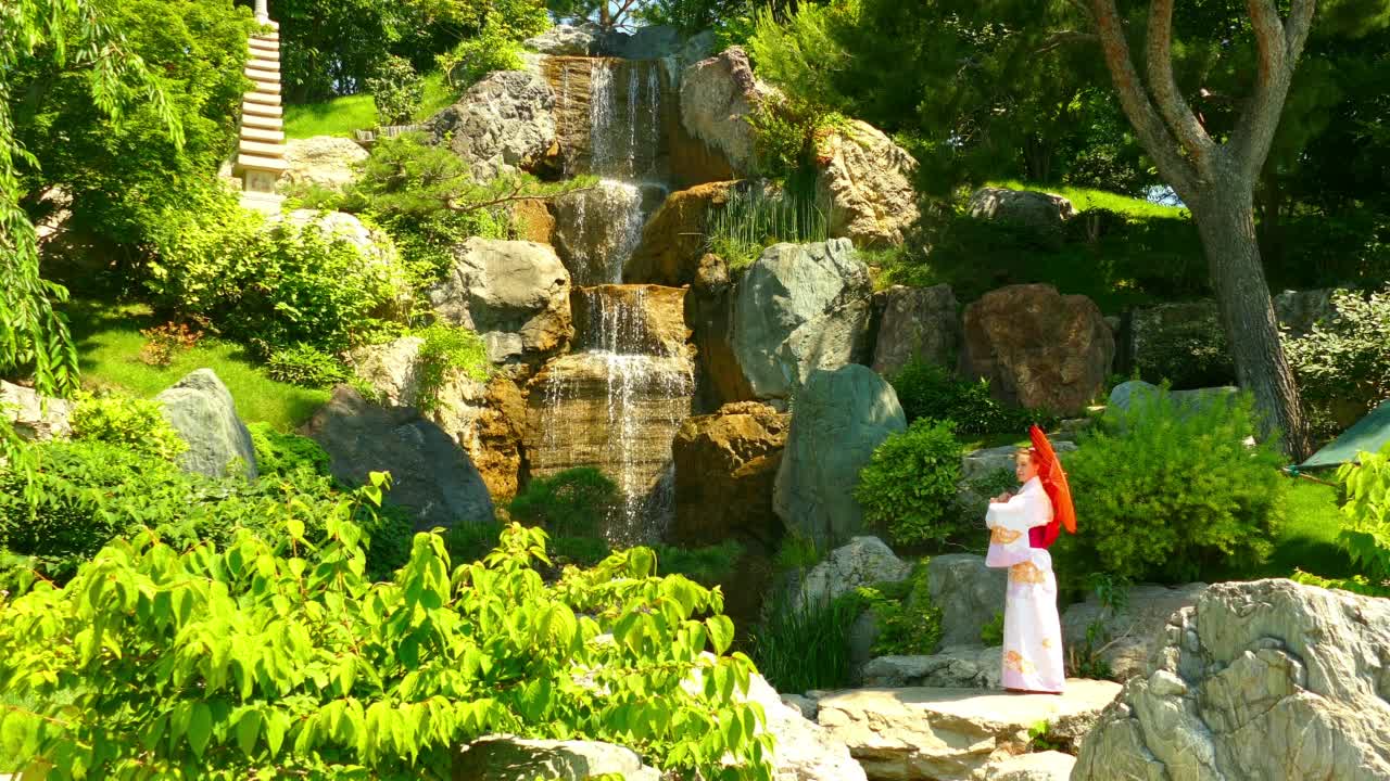 风景——在瀑布附近的日本花园中，一位穿着和服的美丽女子视频下载