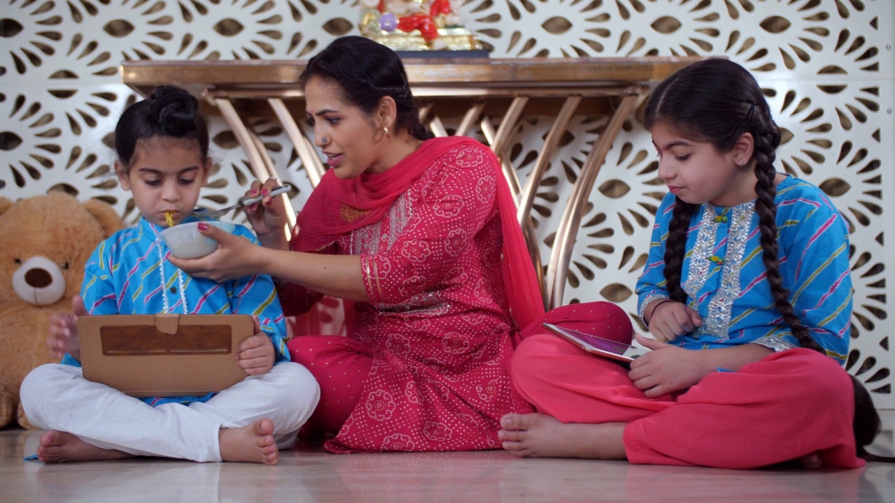 一位印度母亲正在给她的儿子喂面条——用平板电脑、屏幕成瘾、美味的饭菜、在线学习视频素材