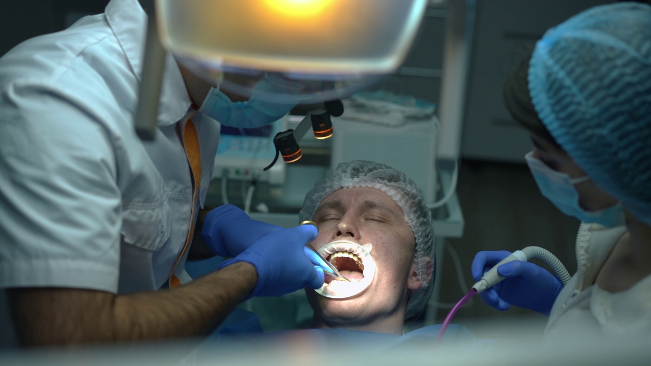 前视图病人在牙科椅与外科医生缝口腔牙龈在慢动作。白人男子在医院室内正畸诊所接受牙科手术。口腔学的概念。视频素材