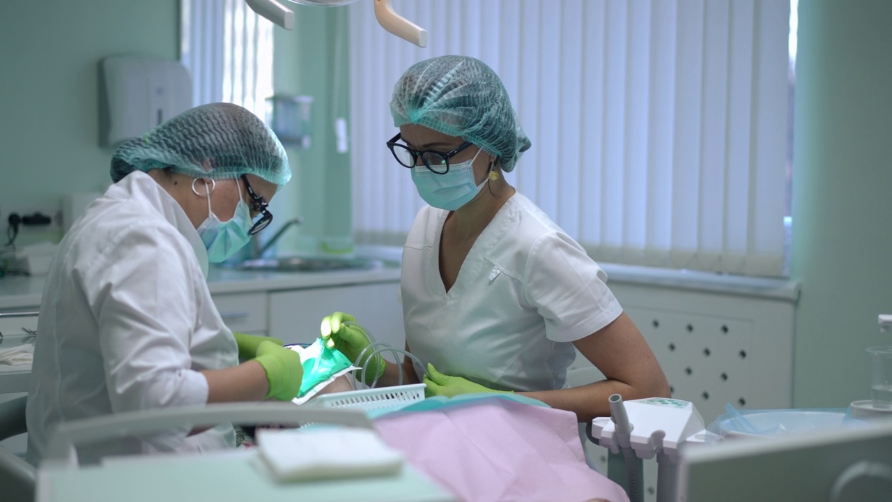 集中白人牙医和助手检查坐在牙科椅上的病人牙齿。专注的专业医生和护士在正畸诊所治疗患病的女性。缓慢的运动。视频素材