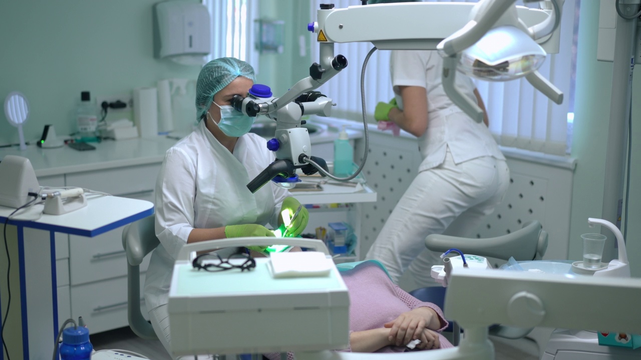 专注于专业正畸治疗牙齿疾病检查龋齿，以牙科显微镜为背景模糊辅助收集工具。白人专家牙医在牙科椅上治疗病人。视频素材