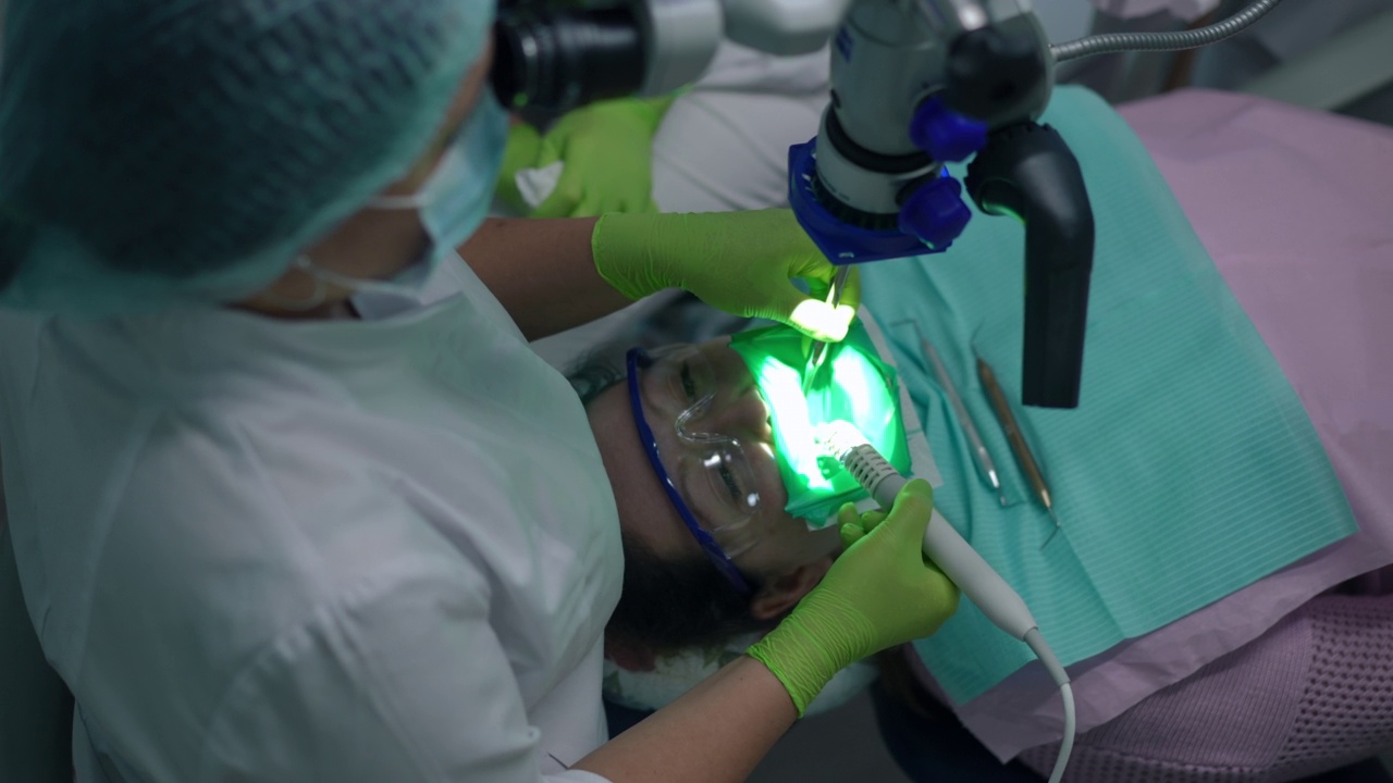 与专业正畸医生在牙科椅上用牙科显微镜检查口腔的俯视图病人。牙髓治疗与保健理念。视频素材