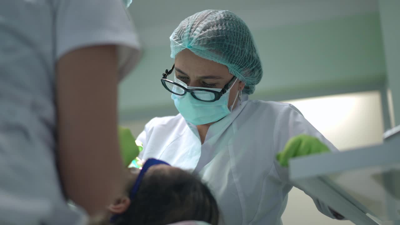 肖像专注的专业白人女牙医在医院室内与病人和助理工作。集中的医生治疗患病的妇女和护士帮助慢动作。视频素材