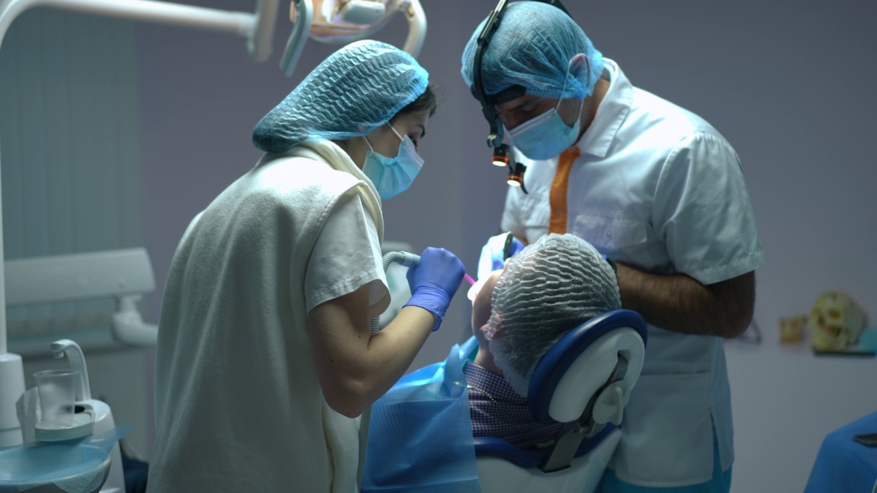 专注于中东女性牙科助理帮助专业牙医清除病人口腔中的唾液。集中的年轻护士协助专家医生治疗坐在牙科椅上的男子。视频素材