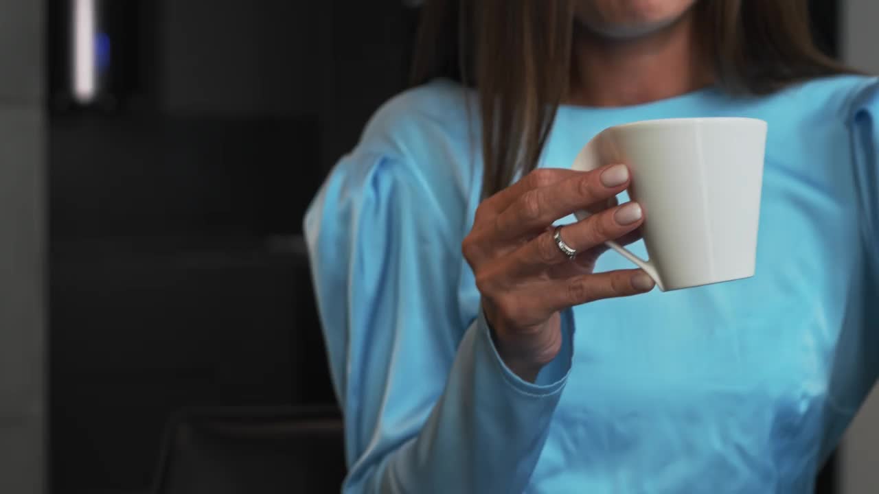 一个穿着裙子的女人坐在桌子旁喝咖啡，拿着白色的杯子，交流视频素材