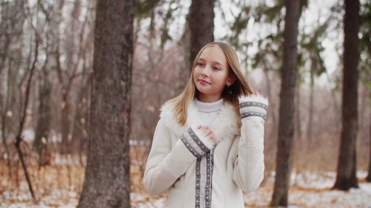 美丽的年轻女子在冬天的森林里抚摸头发。时装模特女人在冬季大衣摆雪森林。视频下载