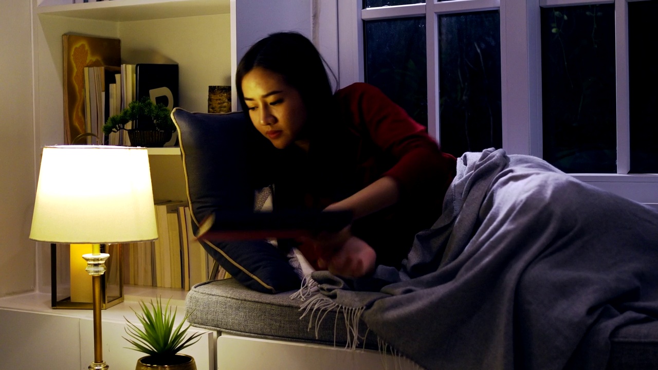 晚上在客厅看书的亚洲女性。生活方式和放松在家里。视频下载