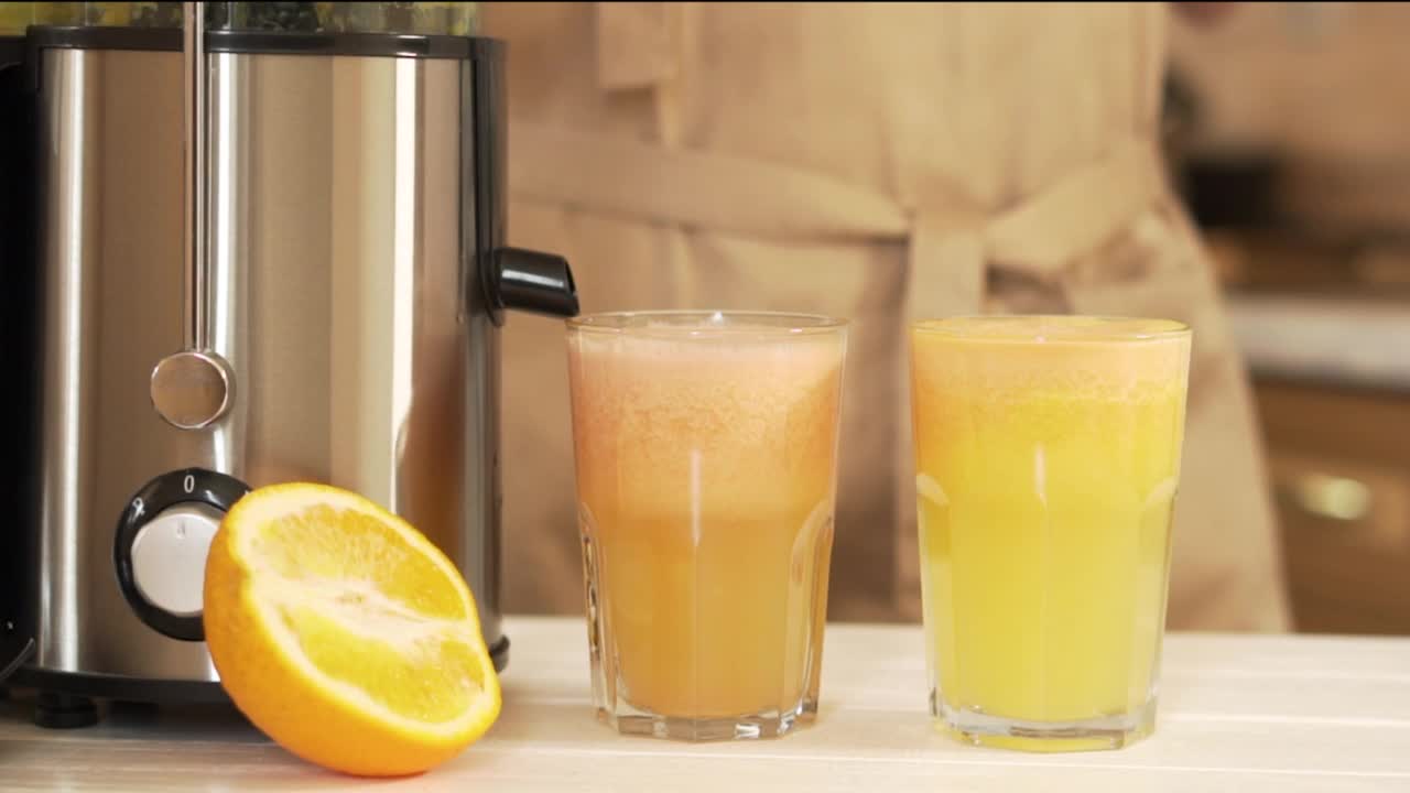 一个女人的手拿着两杯在榨汁机里准备好的新鲜果汁。柚子和橙汁是健康的食物，是节食和排毒的水果。在大热天为全家人准备一杯饮料视频下载