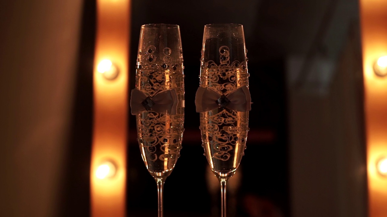 桌子上放着两个装饰华丽的带有气泡的婚礼香槟杯，背景是模糊的黄色灯光。近距离视频素材