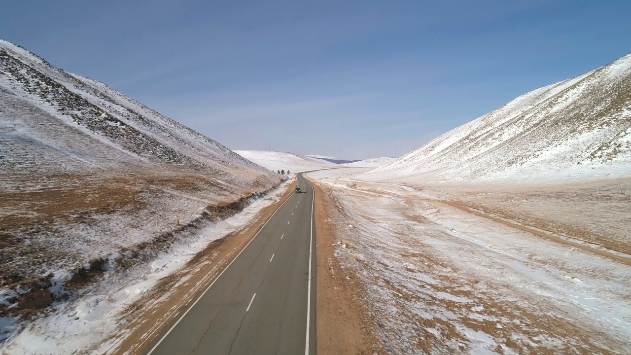 在雪山之间的公路上的鸟瞰图，一辆汽车在蓝天下行驶。视频下载