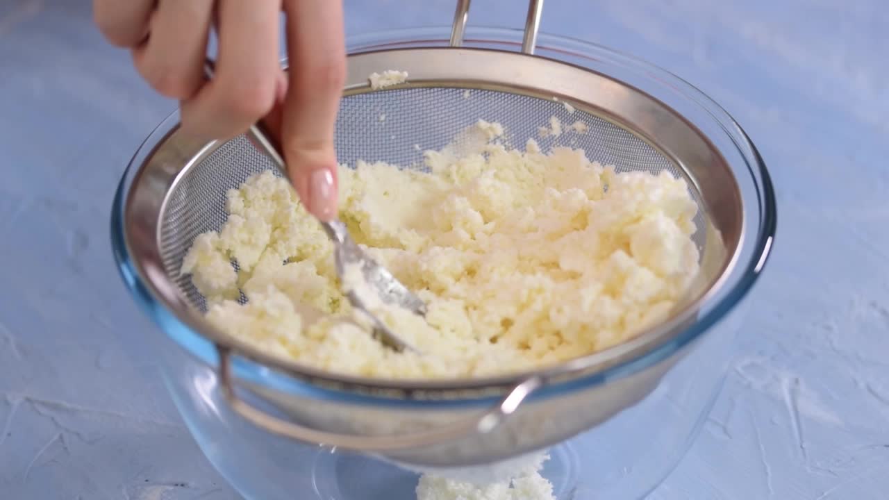 女人在家里的厨房里用筛子擦干酪。视频下载