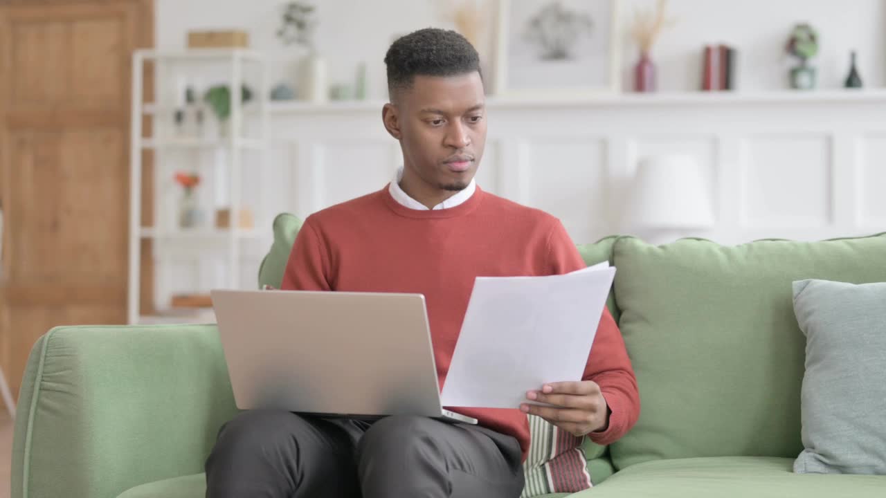 非洲人拿着笔记本电脑在沙发上看文件视频素材