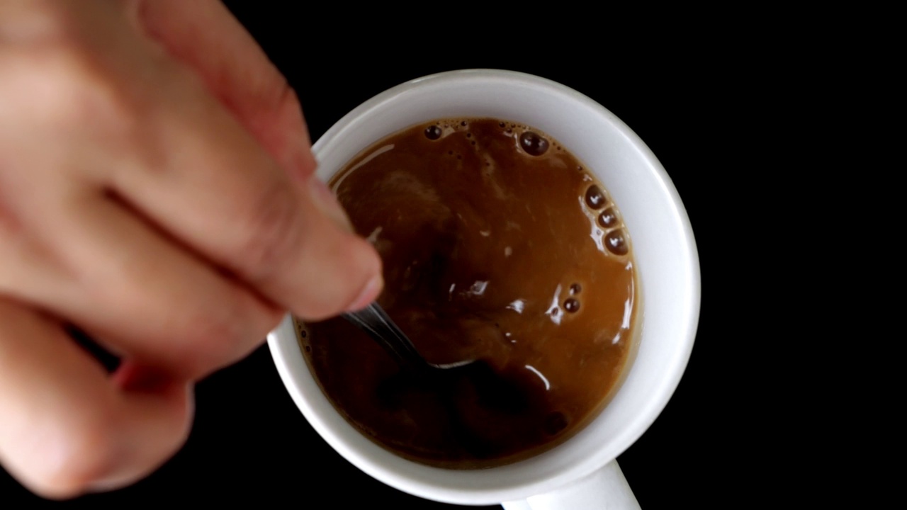 俯视图慢动作视频图像，一个女人的手在一个白色的杯子里煮热咖啡，黑色背景-4k视频素材
