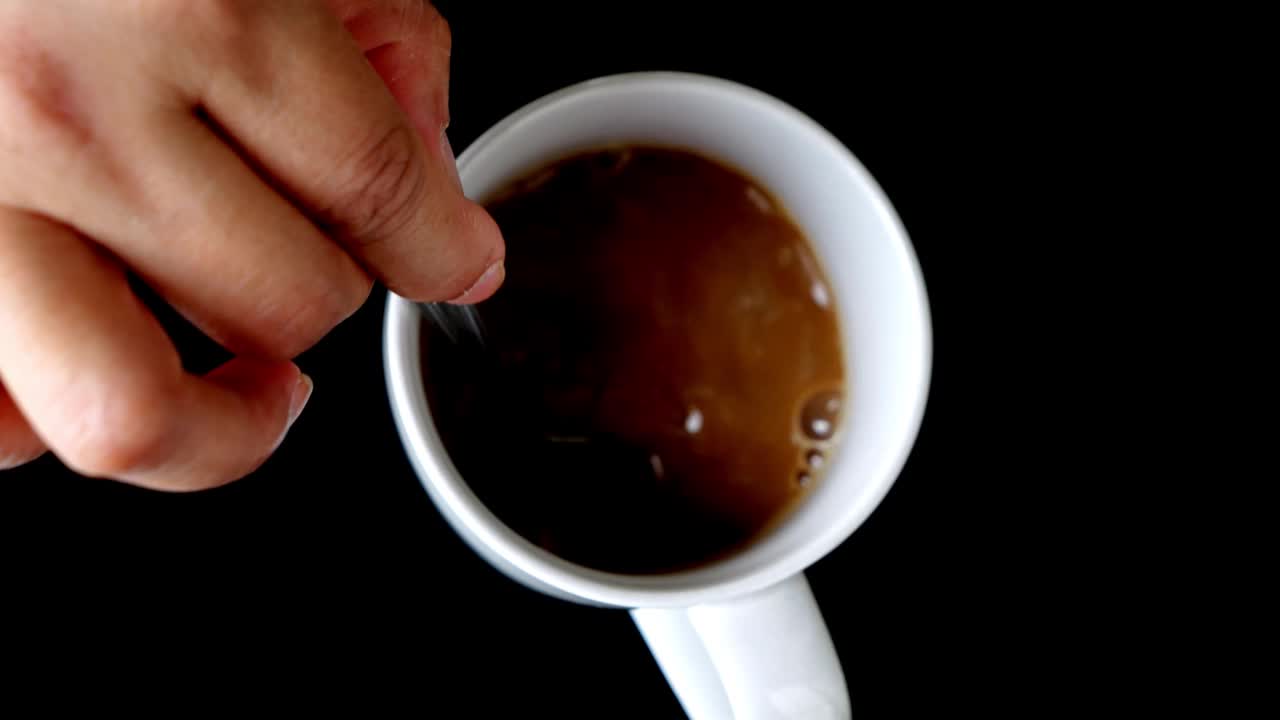 俯视图慢动作视频图像，一个女人的手在一个白色的杯子里煮热咖啡，黑色背景-4k视频素材