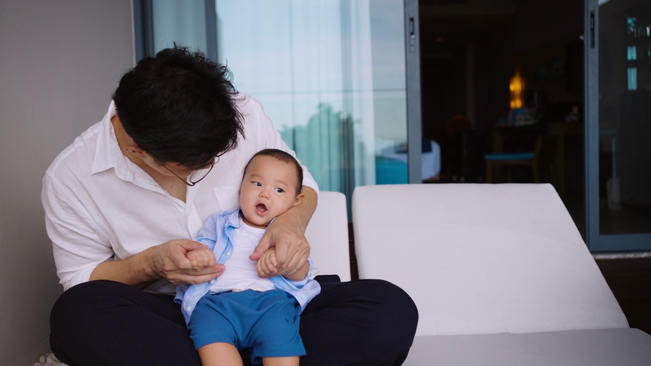 父亲坐着和可爱的新生男婴玩耍。单亲家庭，真实的生活方式养育父亲亲吻和抱着他的儿子的时刻。视频下载
