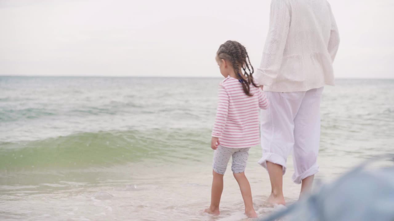 母亲和小女儿在海边散步海滩上幸福的一家人母亲牵着孩子的手在海边散步。暑假旅行视频素材