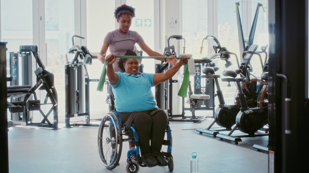 帮助残疾人运动员康复和轮椅康复的理疗师。私人教练为残疾超重女性患者做弹力带运动，以提高其灵活性和力量视频下载